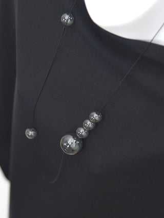 A mannequin wearing a black shirt and a long wire necklace with six glass orbs in various places.