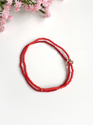 A pair of red beaded bracelets, held together by a small gold heart charm.