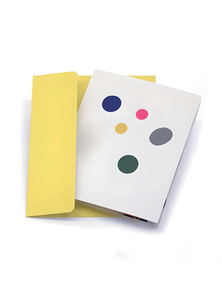 A white greeting card with colorful circle cutouts, in front of a yellow envelope.