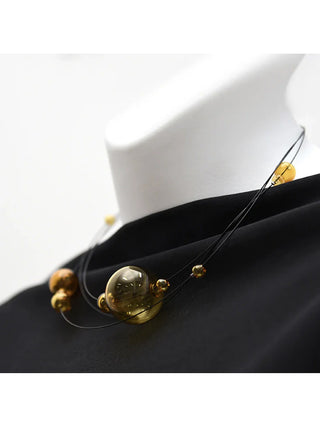 Mannequin wearing a black shirt and a short necklace with black wires holding amber glass orbs of various sizes.