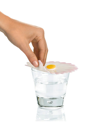 A hand placing a silicone drink cover in the shape of a daisy atop a water glass.