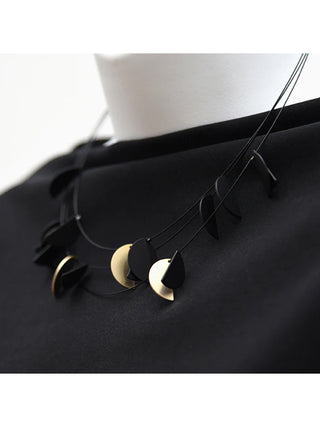 Mannequin wearing a black shirt and a short necklace made of black wire holding gold and black half circles.