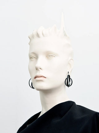 A mannequin wearing a black shirt and earrings made of black rings and a glass orb.
