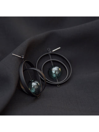 A pair of post earrings made of two black hoops and a glass orb in the center.