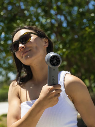 A woman cooling off with the gray eVENT fan on a sunny day.