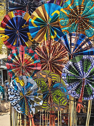 A collection of vibrantly colored fabric fans displayed on a wall outside.