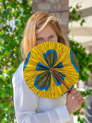 A woman outside holding a yellow and blue fabric hand fan.