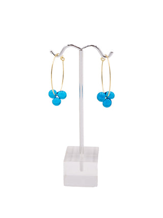 A pair of gold hoop earrings with a cluster of three blue glass spheres, hanging on a silver earring stand.