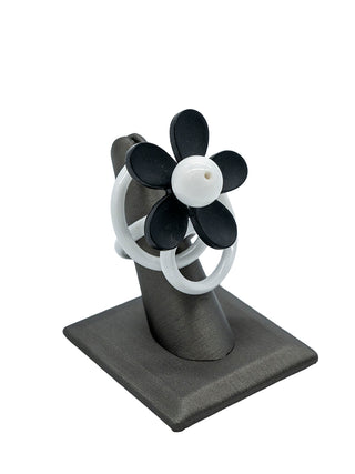 A white squiggle ring with a black and white flower, displayed on a gray ring holder.