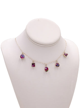 A necklace display holding a charm necklace with five differently shaped charms, all made with real flowers.