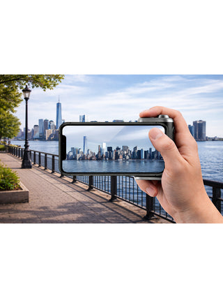 A hand holding a smartphone with the Magshutter Pro attached in landscape mode, taking a picture of a city skyline.