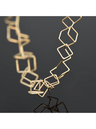 A close-up of a gold bracelet made with linked cube-like pieces.