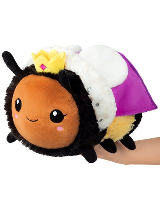 A smiling, plush version of a queen bee complete with crown and robe, being held up by a hand.