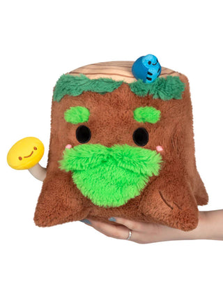 A brown tree stump with a green moss beard and eyebrows, with a yellow mushroom and a blue bug, sitting on a hand.