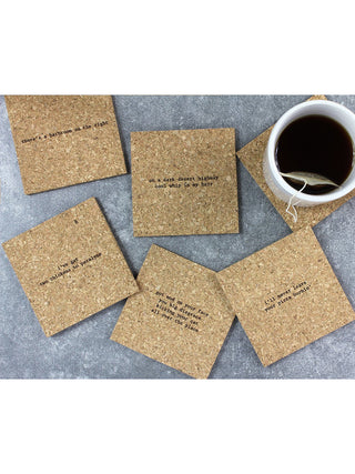 6 cork coasters with mistaken lyrics from classic rock songs spread out on a table with a cup of tea.
