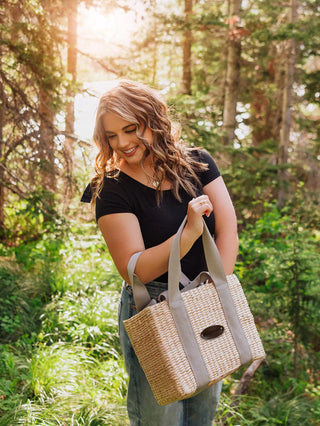 A woman holding the Ravinia woven picnic basket in a forest.