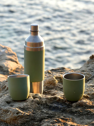 A green wine flask with the two magnetic tumblers by its side, sitting on a rock.