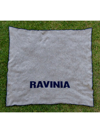 A pewter-toned knit blanket with a navy whipstitch border and Ravinia in navy lettering.