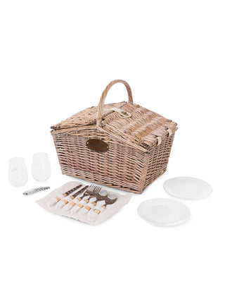 A wicker picnic basket with a leather plate with the Ravinia logo, closed, with 2 plates, 2 wine glasses, a corkscrew, and 2 sets of utensils laying in front.