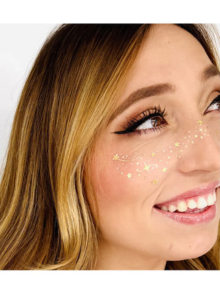 A close-up of a person's face with gold sparkly face stickers over their cheeks and nose.