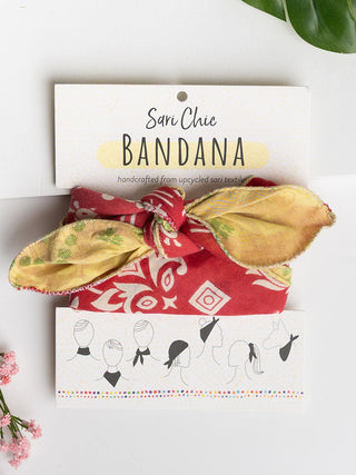 A red and yellow patterned bandana made of saris tied around a cardboard card with different styling options and the words Sari Chic Bandana.