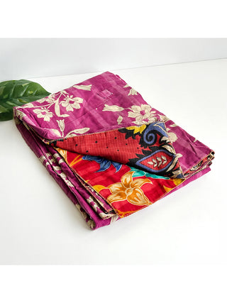 A folded colorful patchwork blanket made of saris with the corner folded to show different patterns, on a white table.