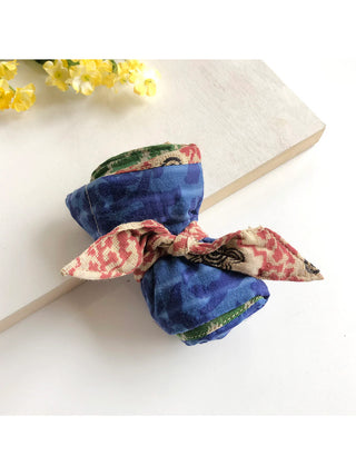 A colorful tote bag made from saris, rolled compactly, on a white table.