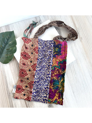 A colorful tote bag made from saris laying on a wood table next to a leaf.