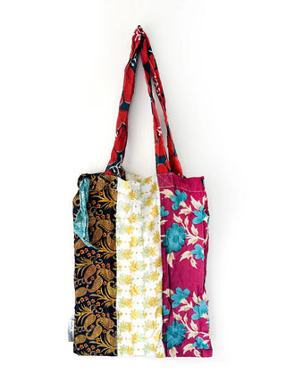 A colorful tote bag made from saris hanging on a white wall.