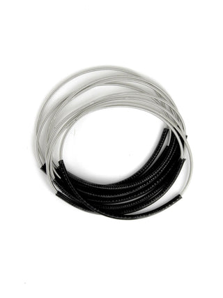 A set of silver piano wire bracelets with black sleeves.