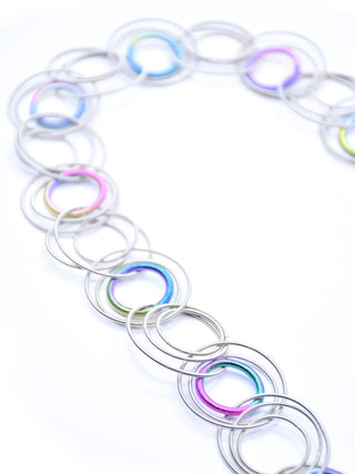A close-up of a silver and rainbow necklace made of multiple interlocking rings of piano wire.