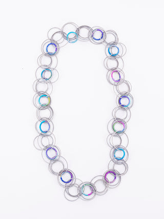 A silver and rainbow long necklace made of multiple interlocking rings of piano wire.