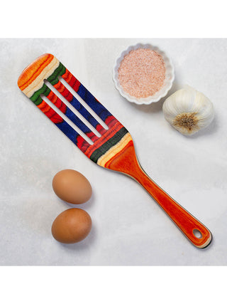 A colorful slotted flat kitchen utensil on a countertop near some ingredients.