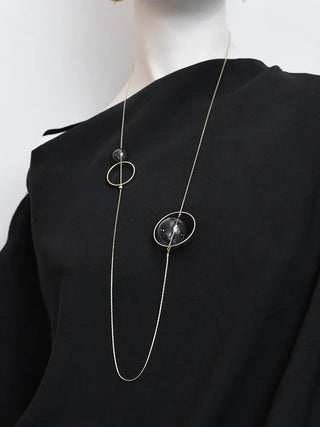 A mannequin wearing a black shirt and a long necklace with metal rings and glass beads, adjustable.