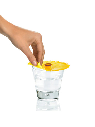 A hand picking up a silicone sunflower drink cover covering a glass filled with water.