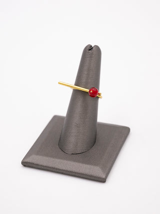 A brass ring with a red glass ball on one end on a gray ring holder.
