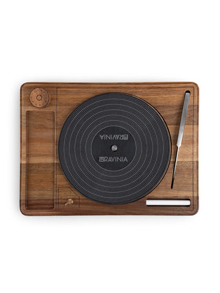 A wooden cheese board that looks like a turntable with a slate Lazy Susan center, a stainless steel knife, and a piece of chalk.