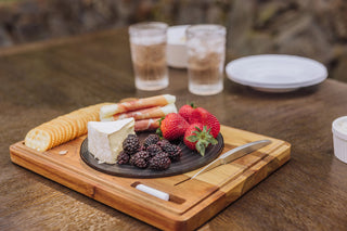 A wooden cheese board that looks like a turntable with a cheese spread, and two glasses and plates on a wooden table.