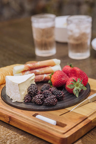 A wooden cheese board that looks like a turntable with a cheese spread, and two glasses on a wooden table.