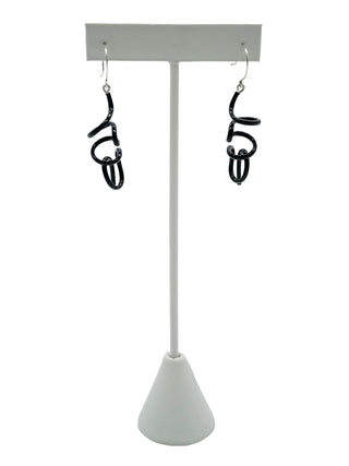 Black twisty earrings hanging on a white earring holder.
