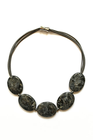 A necklace laid flat, with strands of silver wire above and five large slate-colored oval stones below.