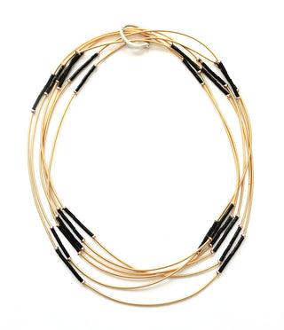 Overhead view of a golden piano wire necklace with black beads, and a ring claps.