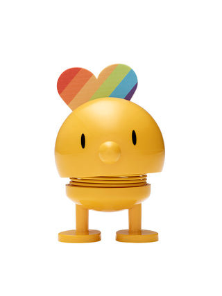 A smiling yellow figure with a spherical head and spring in its middle, with rainbow attached to the back of its head.
