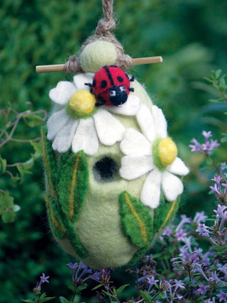 A felt birdhouse in the wild, decorated with leaves, flowers, and a large ladybug.