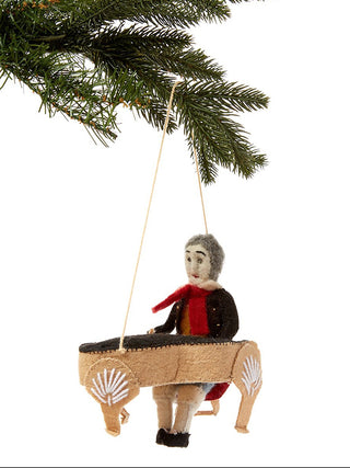 A holiday ornament depicting Beethoven playing a piano, hanging from a tree.