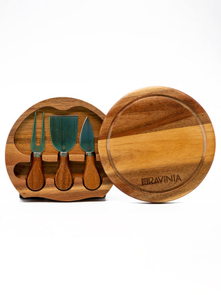 A two-level circular wooden cheeseboard swiveled open to reveal the three small cheese knives that are housed inside. The side on the right has the Ravinia name and logo on it.