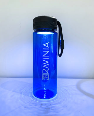 Blue water bottle with Ravinia on its side, the flashing on top lit, dispersing light around the bottle.