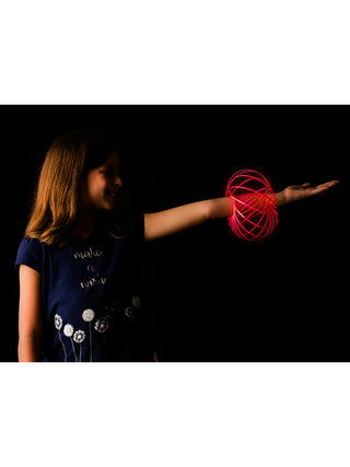 Profile view of a girl against a black background, a sphere of pink rings around her wrist as she holds her arm out.