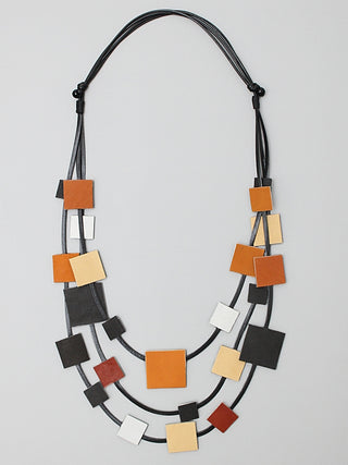 this necklace features multiple strands of black cord with square leather pieces in shades of brown and black, strung throughout. 
