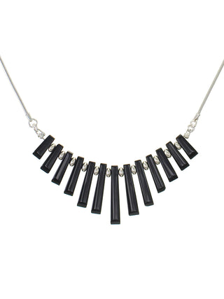 A necklace's pendant of tapered black onyx pieces, with the middle ones being larges, hanging from a silver-toned chain.